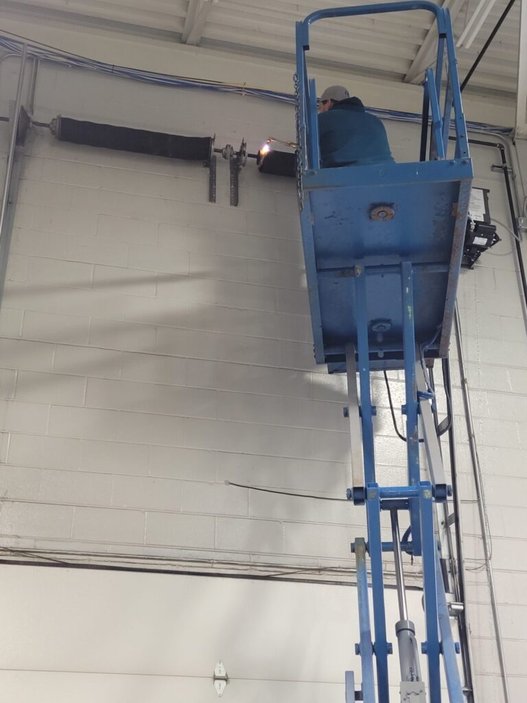 Garage door chain off track slipping in St Charles IL: a technician on a blue lift platform performing maintenance or repair